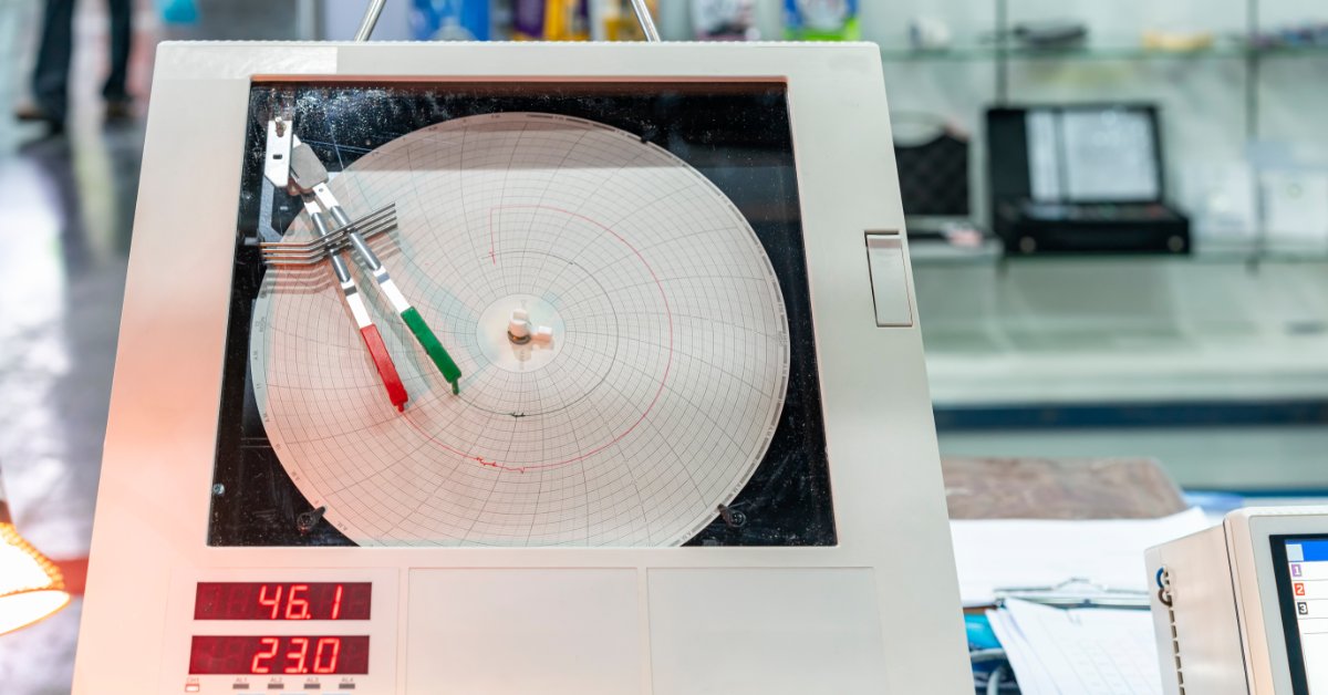 A circular chart recorder with red and green pens, a paper graph, and digital readings displayed on laboratory equipment.