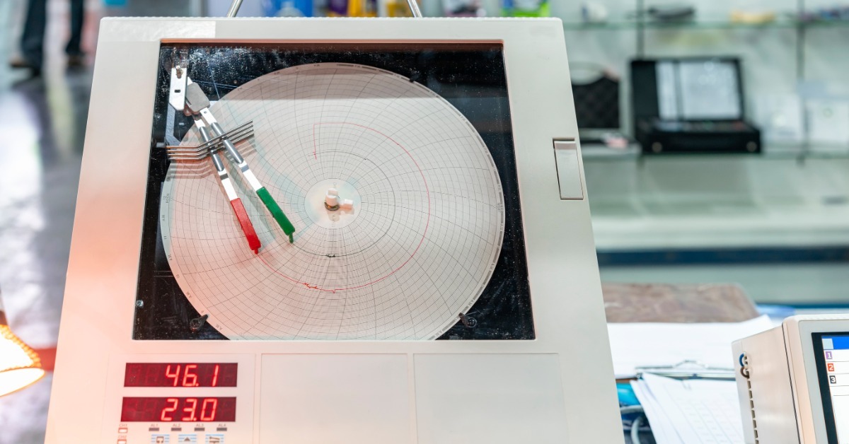 A circular chart recorder with red and green pens tracing measurements on graph paper, with digital displays below.