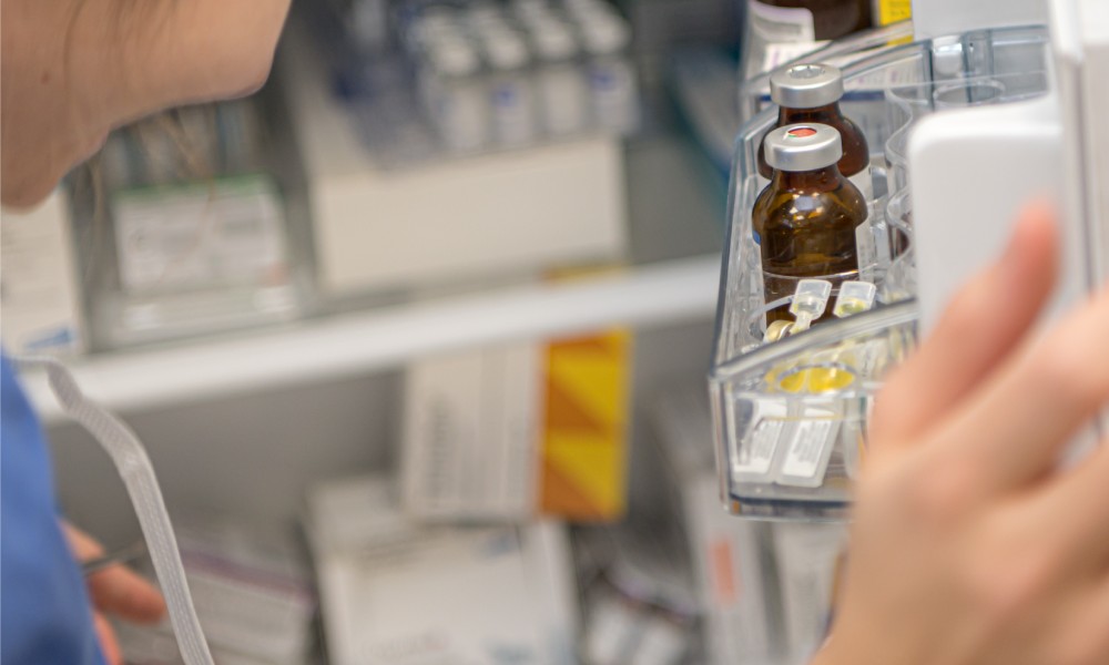 A female pharmacist examines the wide variety of medications stored in a fridge to provide a patient with their prescription.