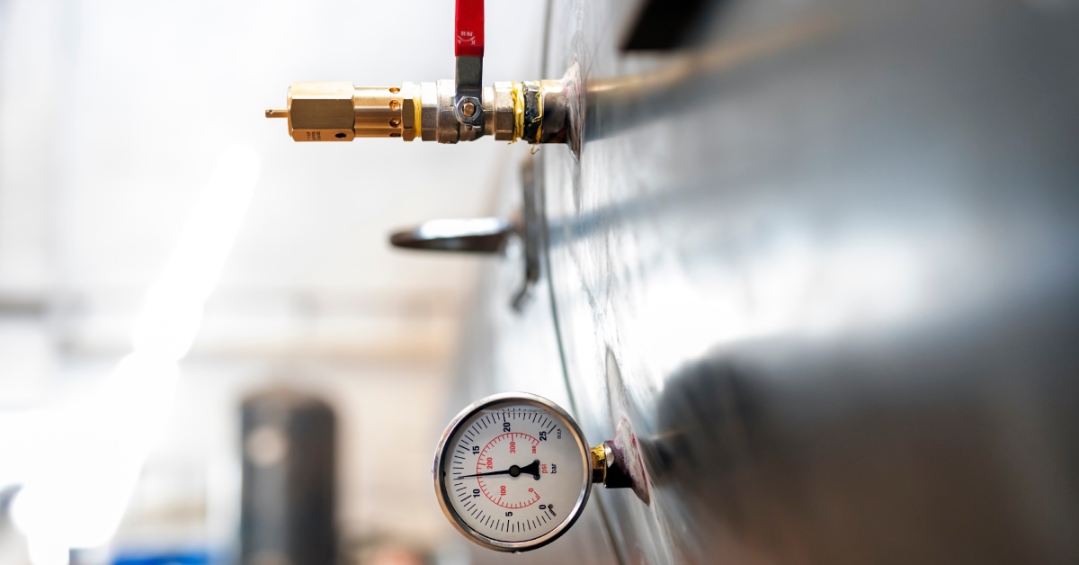 A cylindrical tank indoors with a safety valve and pressure meter. The background includes blurred scientific tools.