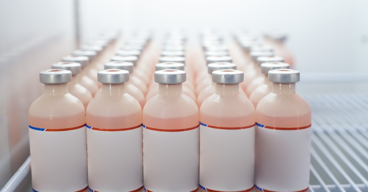 Several rows of vaccine vials with white, red, and blue labels lined up neatly on a refrigerator shelf.