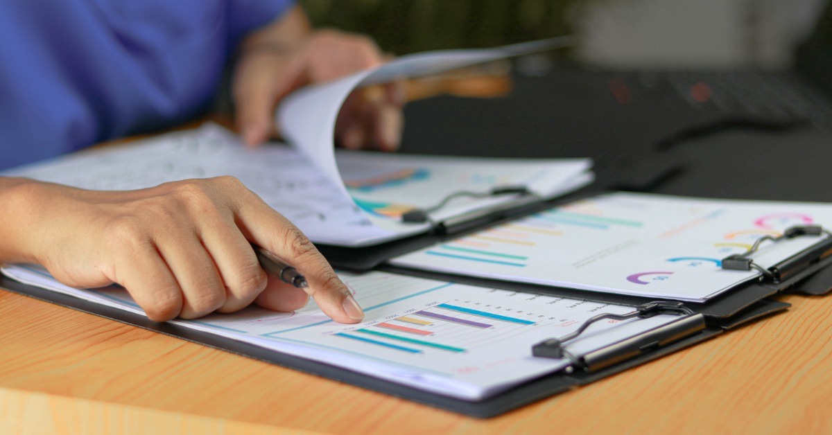 A close-up of a person sitting at a desk while reviewing various sets of papers displaying different charts and graphs.